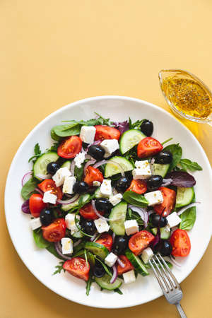 Greek salad of fresh cucumber, tomato, red onion, feta cheese and olives with olive oil. Salad with vegetables and greens. Healthy food, top viewの写真素材