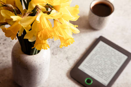 Modern ebook reader, daffodils flowers on background. Top view, minimal flat lay style composition. Women desk, fashion blogger, beauty technologyの写真素材