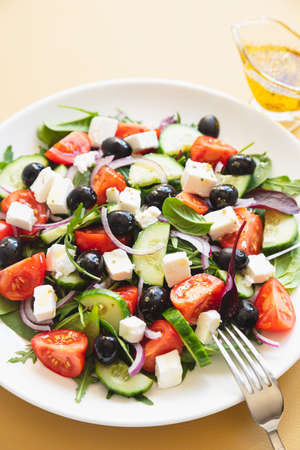 Greek salad of fresh cucumber, tomato, red onion, feta cheese and olives with olive oil. Salad with vegetables and greens. Healthy food, top viewの写真素材