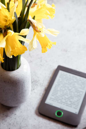 Modern ebook reader, daffodils flowers on background. Top view, minimal flat lay style composition. Women desk, fashion blogger, beauty technologyの写真素材