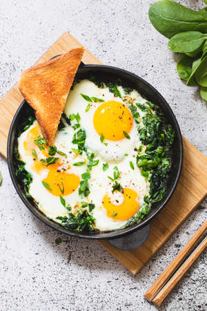 green shakshuka in a cast iron skillet. fried eggs with spinach and fried toast. healthy nutritious breakfast,の写真素材