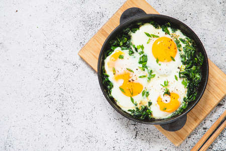 green shakshuka in a cast iron skillet. fried eggs with spinach and fried toast. healthy nutritious...