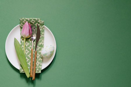 Top view of table setting with plate and napkin near tulip on green table. Easter background.