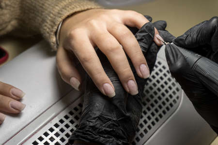 Manicurist master is cleaning pushing cuticle using professional manicure pusher tool, hands closeup.の写真素材