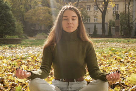 Beautiful young girl meditating in autumn parkの写真素材