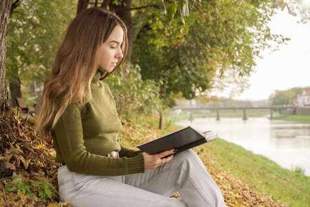 A young girl reads a book on the autumn waterfrontの写真素材