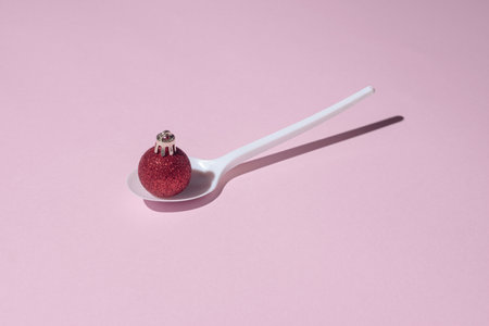 Creative concept made with white spoon and red Christmas decoration. Minimal composition. New Year pastel pink background.の写真素材