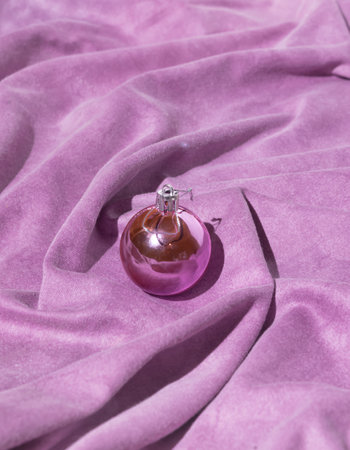 Creative background made with pink Christmas bauble and warm purple silk sheet. Minimal composition. New Year decoration arrangement.の写真素材