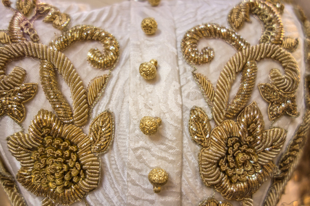 Vintage gold embroidery with floral pattern on an old white dress with gold buttons closeup.の写真素材