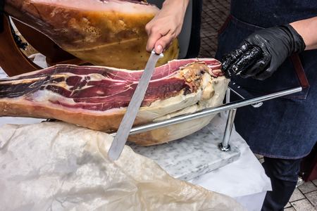 Prosciutto. Traditional Spanish ham on close up. Slicing Hamon iberic. Waiter is slicing jamon prosciutto, selective focus is on cut piece.の写真素材