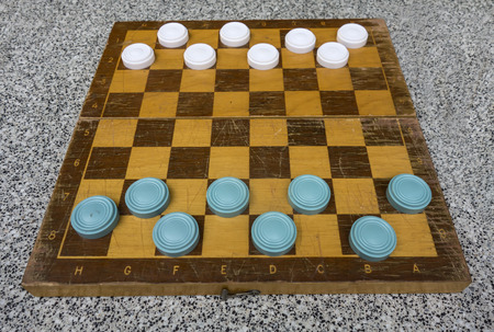 Ancient wooden chess board with blue and white checkers, intellectual game outdoors.