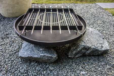 Grill, BBQ, new empty charcoal barbecue close-up. New clean empty roaster stands on the stones. Roaster grate for cooking outdoor.の写真素材