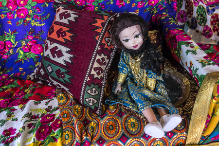 Beautiful doll in a traditional Arabic dress among the embroidered with gold fabrics and bright pillows.の写真素材