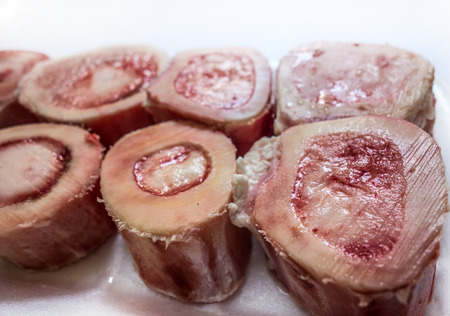 Pieces or slices of big marrowbone with few drops of blood and meat on side. Raw cut into pieces lamb bone with bone marrow inside close-upの写真素材