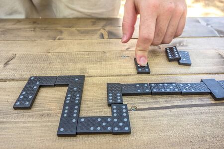 Playing dominoes on a wooden table background . Man's hand on a domino. Domino concept.