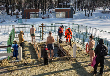 Moscow, Russia, 01/19/2022: Russian people are dipped into an ice hole on the day of the Epiphany. Epiphany bathing in the ice hole in winter. Undressed people in ice water.Traditional ice swimming in Orthodox church Holy Epiphany Day.のeditorial素材