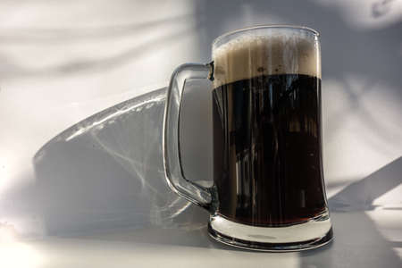 Mug of dark beer with foam on a white background. A delicious pint of lager.の写真素材