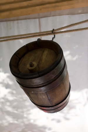 Old wine barrel with iron rings is suspended from a metal hook under a canopy. A beautiful...