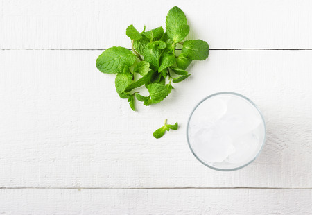 Ice in a glass and fresh mint on a white wooden background. Top view.の写真素材