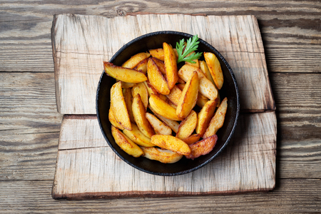 Fried potatoes wedges in a pan on wooden table. Top view.の写真素材