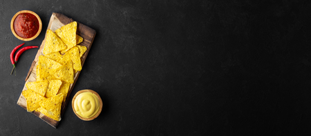 Traditional Mexican food corn chips nachos with salsa and cheese sauce on black background. Banner format. Top view with copy space.の写真素材