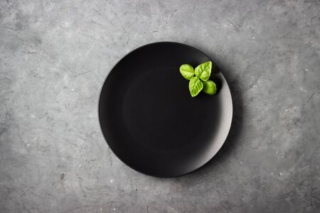 Table setting. Black plate and basil leaves over gray concrete background.の写真素材