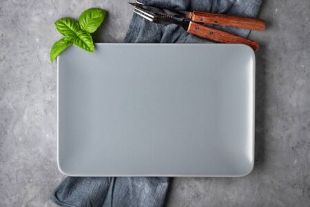 Concept for menu or recipe. Gray empty rectangular plate, cutlery and napkin over concrete background.の写真素材