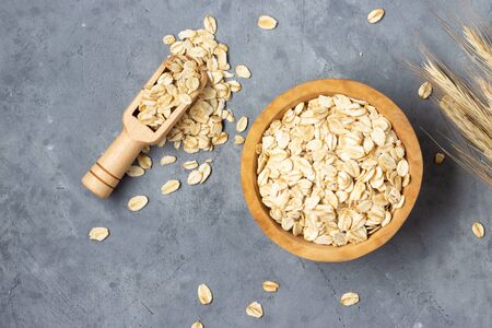 Oatmeal flakes in a wooden bowl on a gray concrete background. Top view.