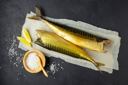 Smoked fish mackerel or scomber on a white parchment paper. Black or dark stone background. Top...