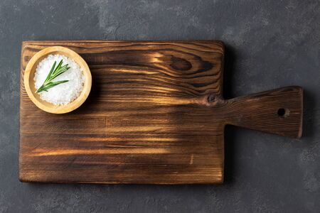 Cooking concept. Vintage cutting board with salt on dark stone background. Copy space.の写真素材