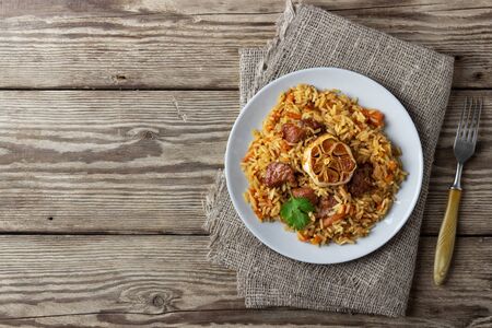 Oriental cuisine. Uzbek pilaf or plov from rice and meat. Wooden rustic background. Top view vith...