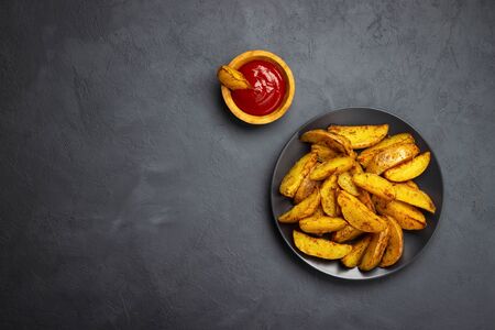Baked potato with spices and ketchup in a black plate. Dark background. Top view with copy space.の写真素材