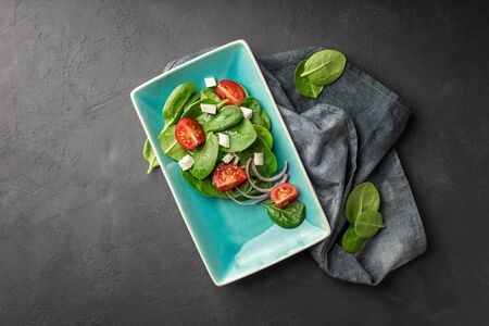 Above view of a fresh green vegetable salad of spinach, tomato and sesame seeds on a blue rectangular plate. Black background. Copy space for text.の写真素材