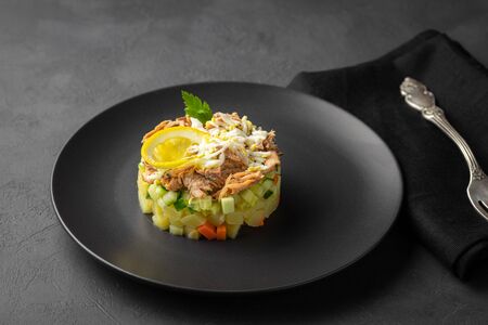 Salad with canned tuna and vegetables in culinary ring on black plate. Dark background. Beautiful serving in the restaurant.の写真素材