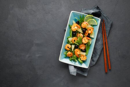 Salad with shrimp, pineapple and fresh herbs in a blue plate on a black background. Healthy food. Top view.の写真素材