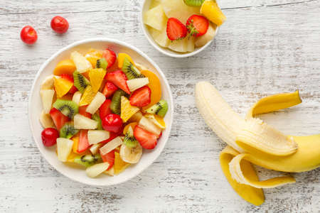 Fruit salad in a plate of chopped strawberries, kiwi, banana, orange and cherry on white wooden...