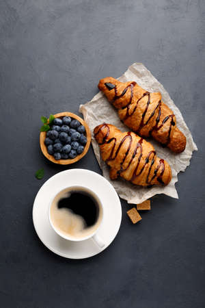 Breakfast - coffee, sweet croissant with chocolate and blueberries. Black stone background. Top view.の写真素材