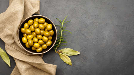 Green olives in a bowl on black (dark) slate background. Top view. Flat lay. Copy space for text.