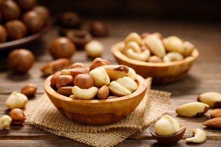 Various nuts in bowl - cashew, hazelnuts, almonds, brazilian nuts and macadamia on a wooden table. Healthy vegetarian food.の写真素材