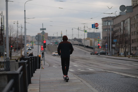 young man riding a scooter on the city street at early morningの写真素材