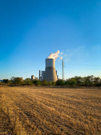 Cooling tower of thermal power plant behind autumn plowed field at duskの写真素材