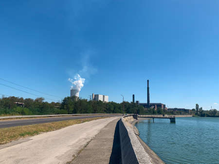 Empty road next to thermal power plant dam with coal facilities and steaming cooling tower at distantの写真素材