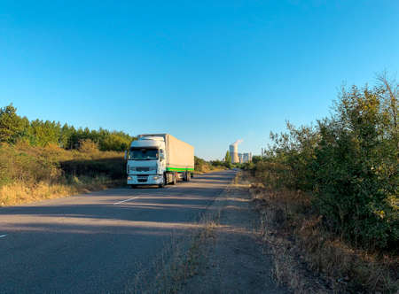 White truck driving on a road at sunset coming from thermal power plant in distantの写真素材