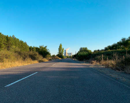Two lanes country road at sunset leading to thermal power plant in distantの写真素材