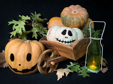 Halloween still life with a pumpkins in a wooden cart and a glowing candle in a bottleの写真素材