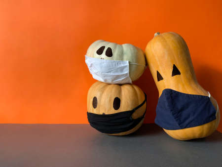 Halloween jack o lantern pumpkins wearing a medical face masks as protection against virus infection and coronavirus or covid-19の写真素材