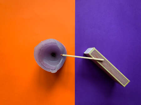 Top view of candle and a matchbox with a matchstick on them against orange and purple duotone backgroundの写真素材
