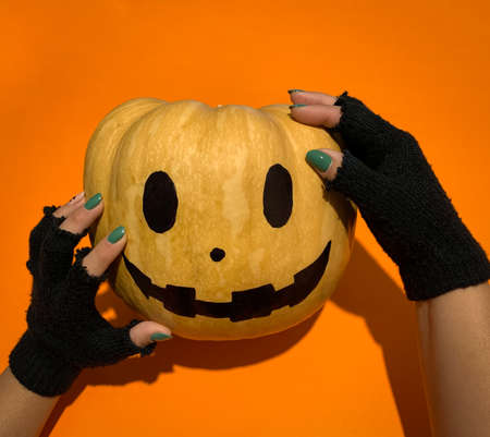Spooky hands with black fingerless gloves over Halloween pumpkin against orange backgroundの写真素材