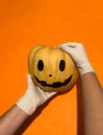 Two hands with white medical gloves carrying Halloween pumpkin in new normal Covid-19の写真素材