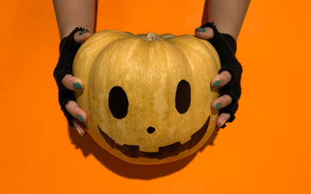 Hands holding jack o lantern Halloween pumpkin on orange backgroundの写真素材